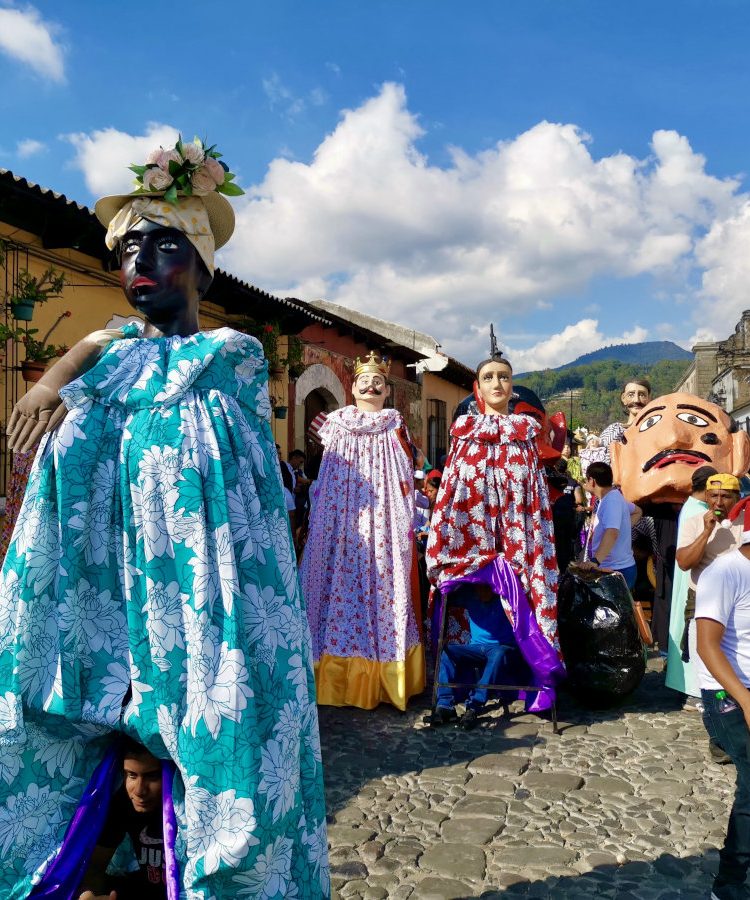 A parade of people in colorful costumes walking down a cobblestone street for Christmas in Antigua Guatemala