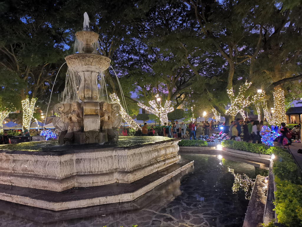 A fountain in the middle of a main square that is light up with lights for Christmas in Antigua Guatemala
