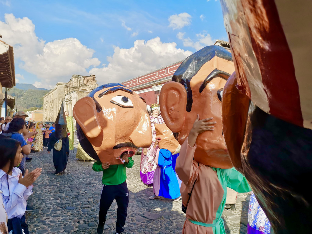 A group of people wearing big paper mache heads while dancing during a parade for Christmas in Antigua Guatemala