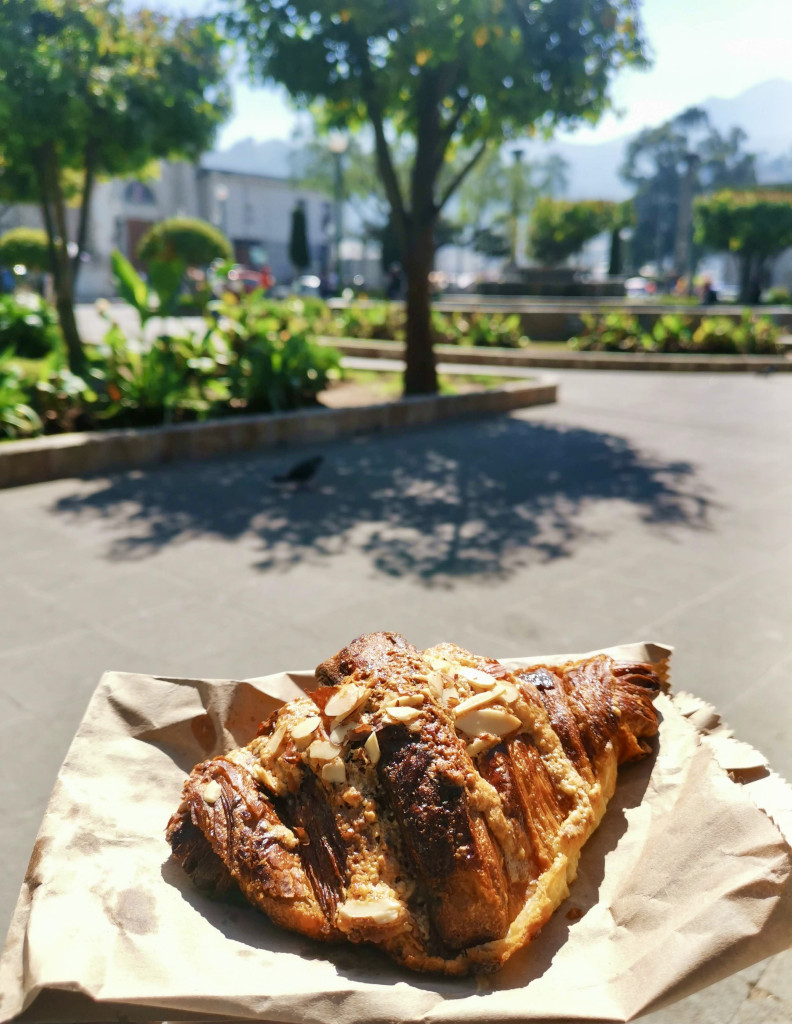 A croissant sitting on a paper bag with Xela's main square in the background