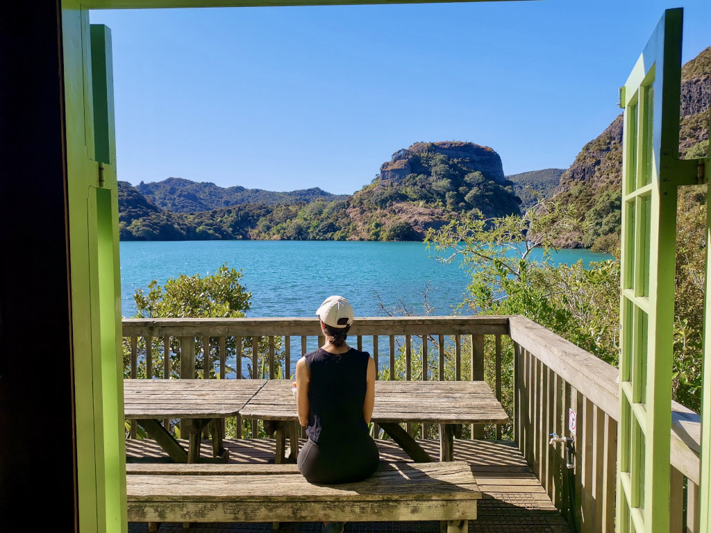 A woman sitting at a wooden picnic table admiring the view over Whangaroa Harbour