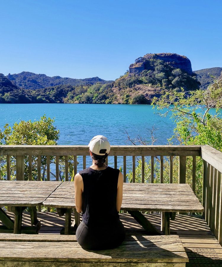 A women sitting on the terrace of Lane Cove Hut overlooking the crystal clear water