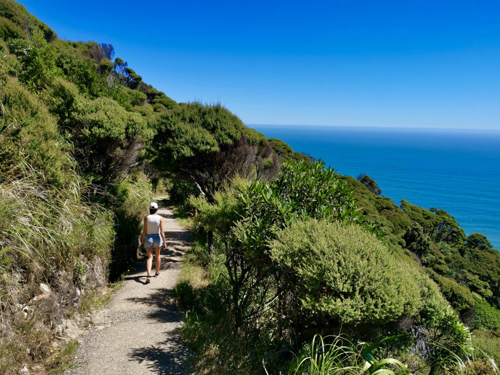 A woman in a white singlet and denim shorts walking along a walking track in West Auckland 