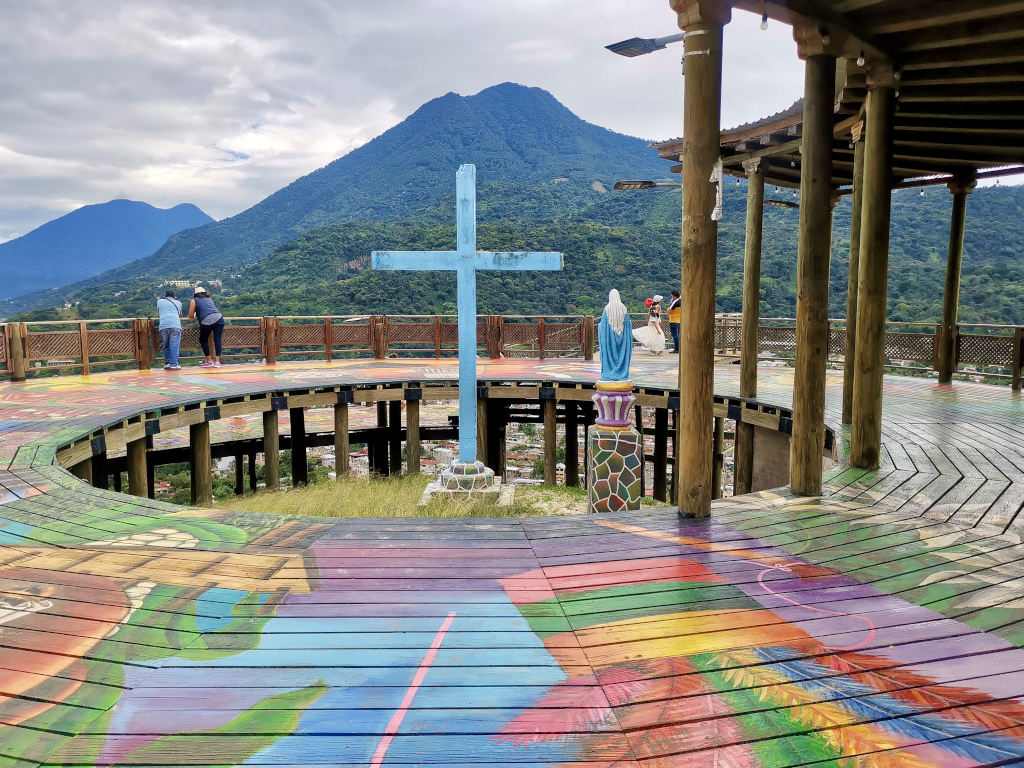 A blue cross in the center of a colorful wooden lookout with views of the volcanoes around Lake Atitlan Guatemala