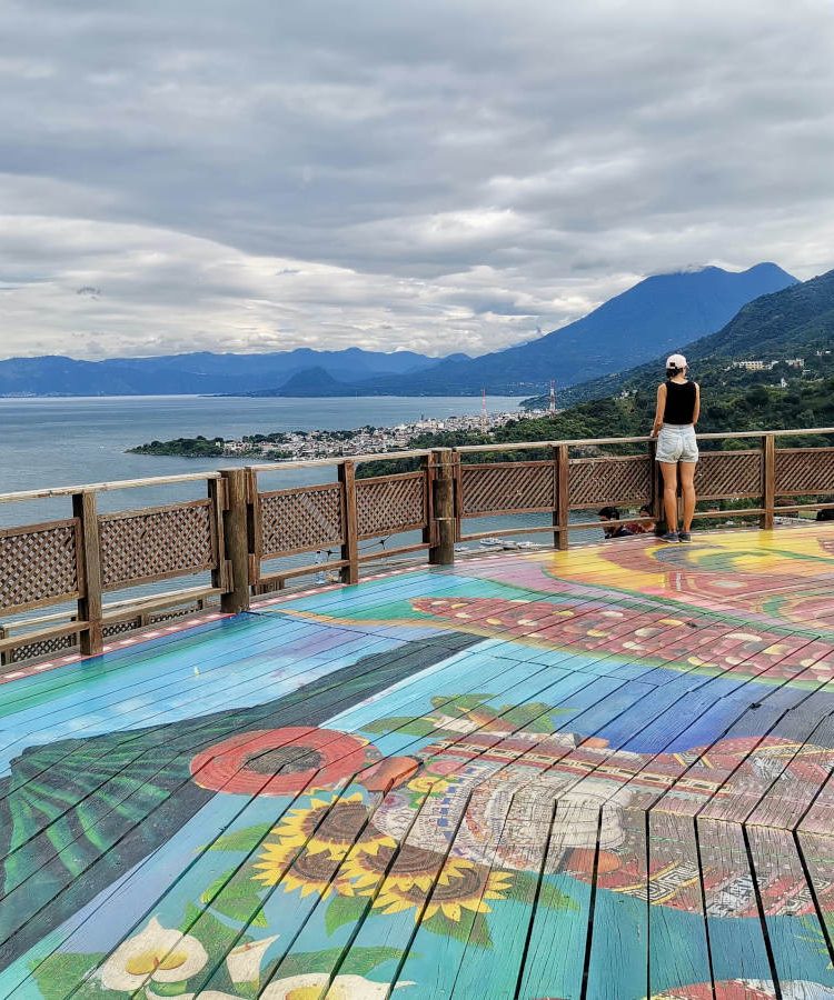 A woman standing on top of the San Juan La Laguna Mirador which is a colorful wooden lookout with spectacular views of Lake Atitlan, Guatemala and nearby volcanoes