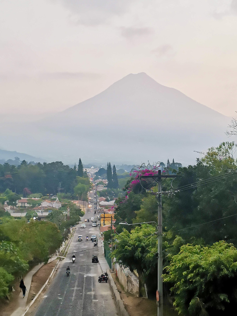 A view of Volcan Agua in Antigua Guatemala with motorbikes and cars driving along a road in front of it