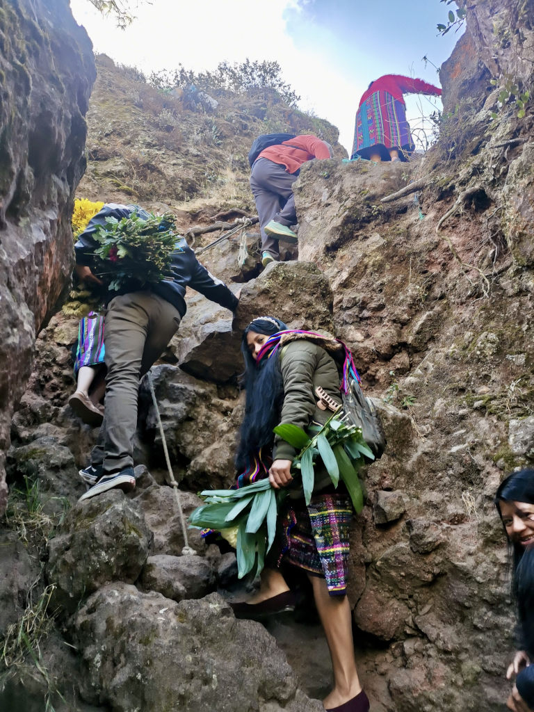 A group of women dressed in traditional Mayan clothing climbing up a steep rocky cliff face