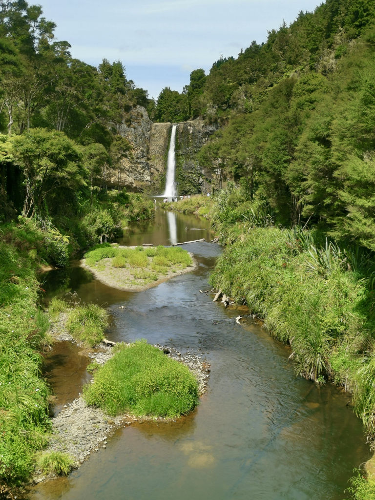 The view of a river with thick green bush on either side and the Hunua Falls at the end of the river