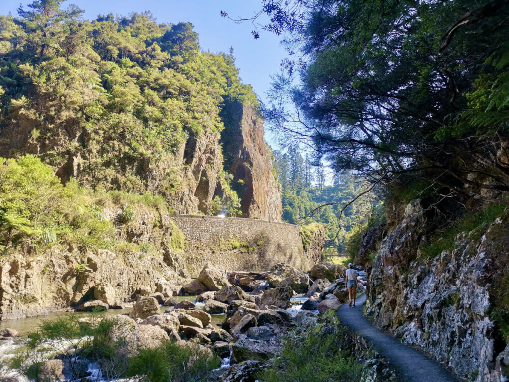 A woman walking along a path next to a rocky river in the Karangahake Gorge