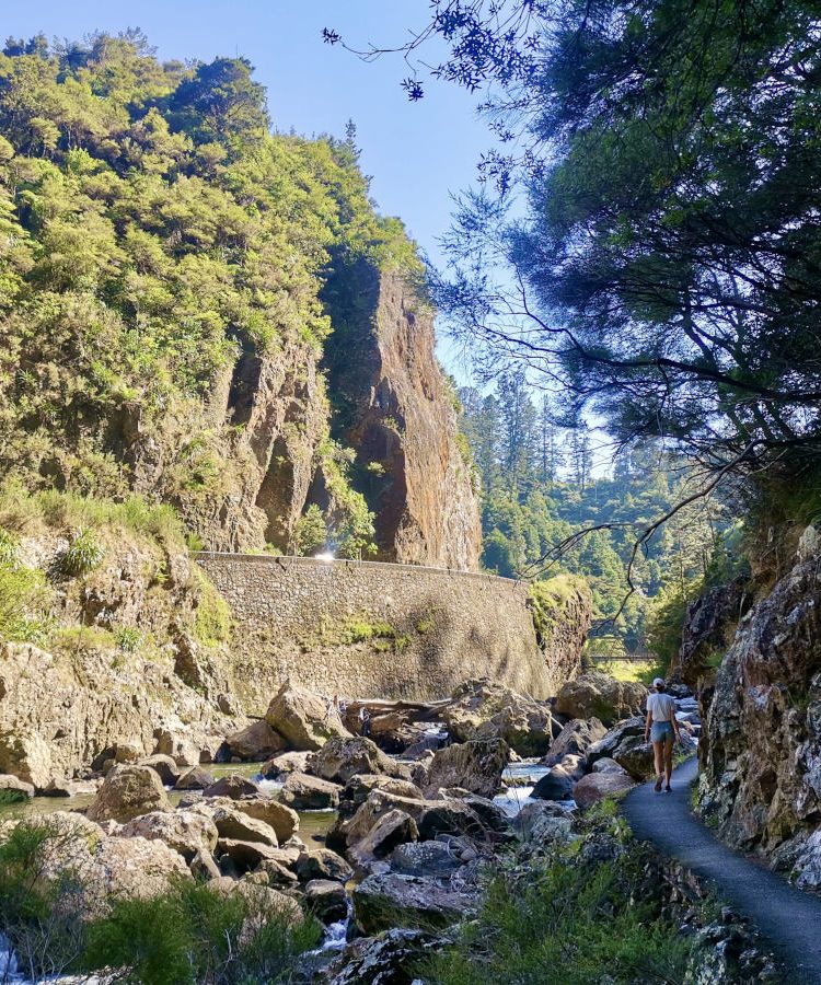 A woman walking along a path next to a rocky river in the Karangahake Gorge