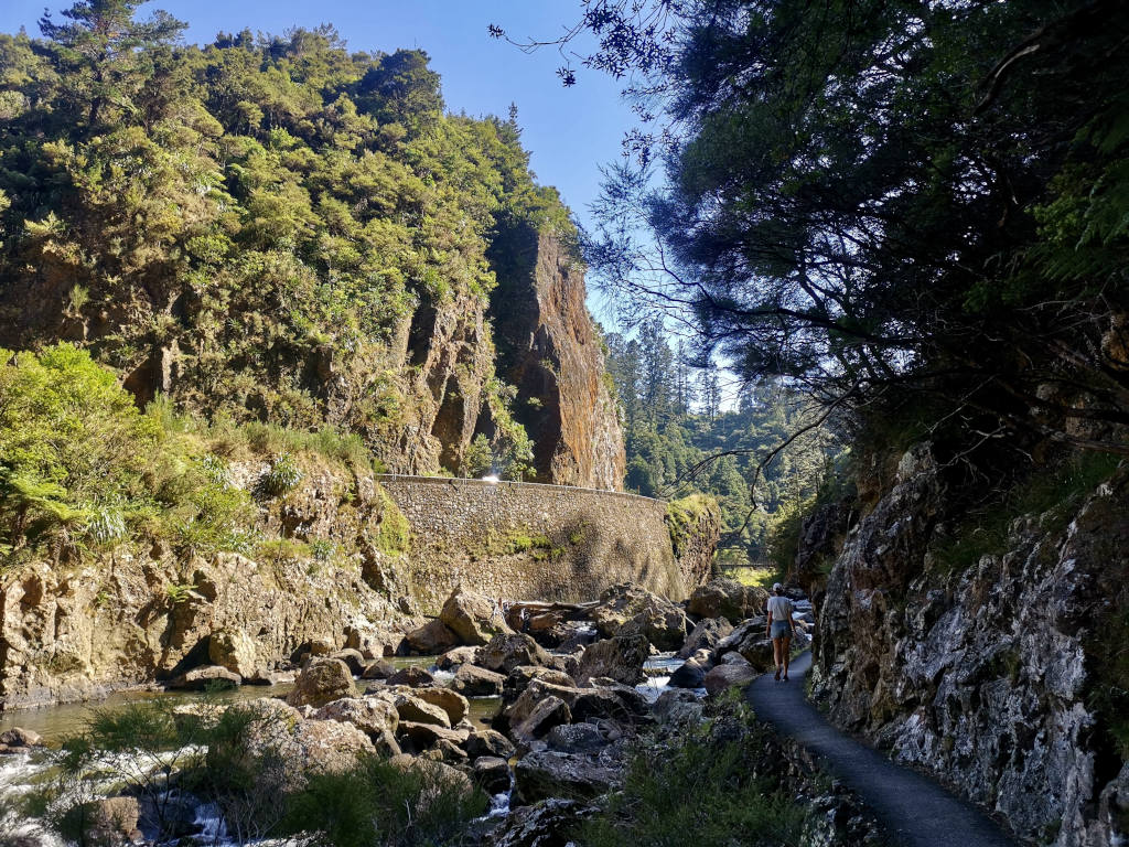 A woman walking along a concrete path on the edge of a river in a gorge in New Zealand