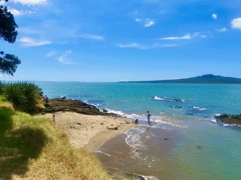 Three people enjoying a beach with a view of Rangitoto volcano in the background
