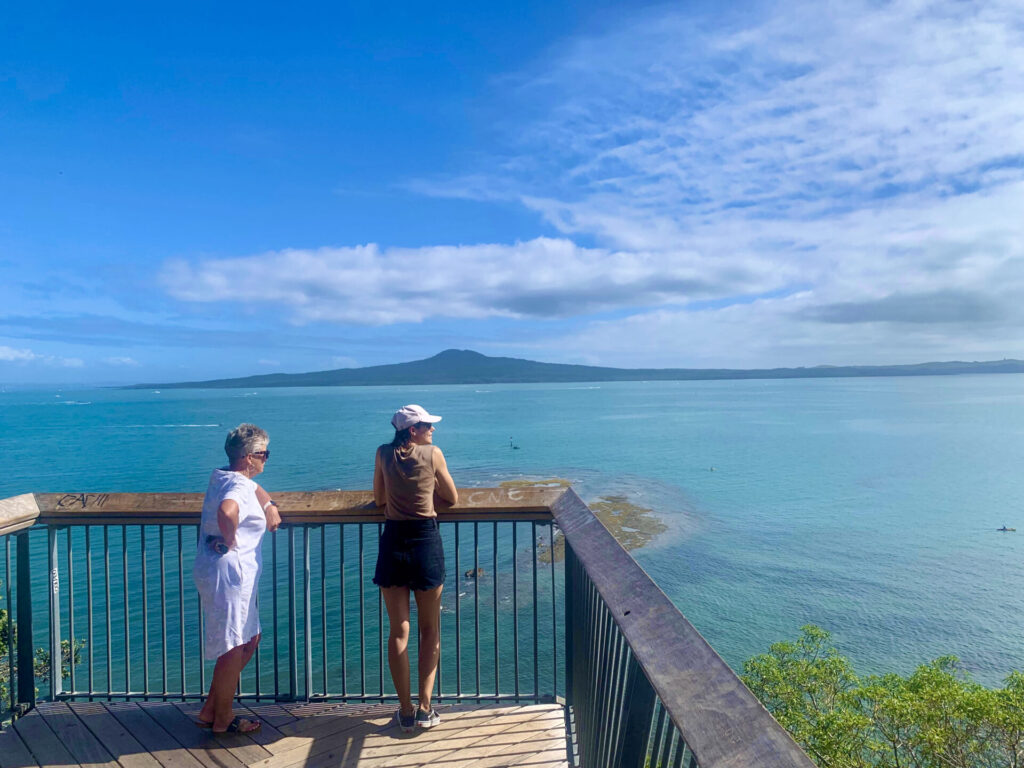 Two woman standing on top of a lookout point overlooking Auckland Harbour with Rangitoto in the distance