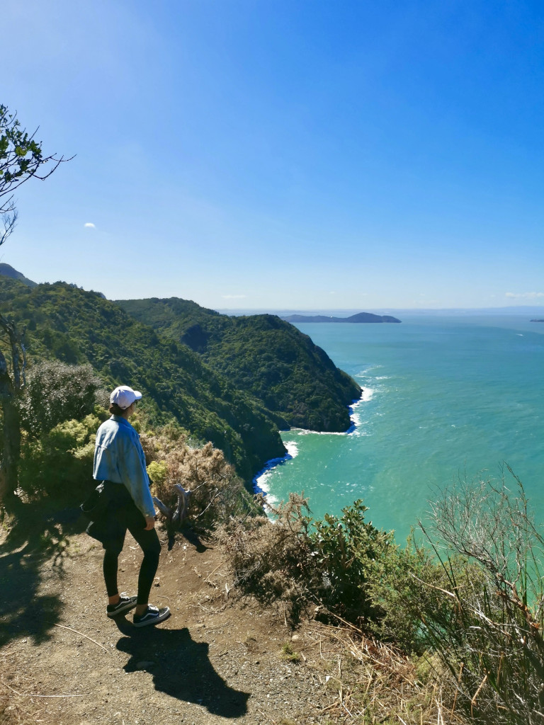 A woman wearing a denim jacket standing next to a cliff top overlooking the Manukau Harbour near Auckland New Zealand