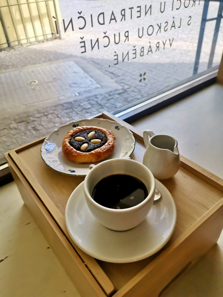 A cup with black coffee sitting next to a pastry on a wooden tray