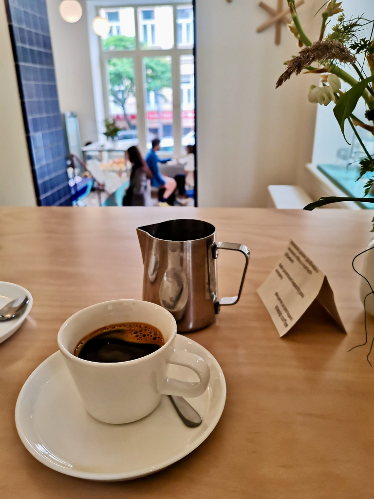 A cup of expresso on a table next to a mettalic jug in One Sip Cafe that has some of the best coffee in Prague