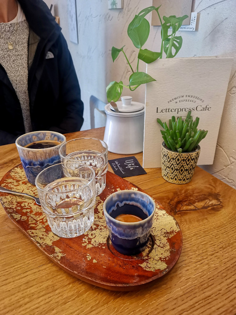 Two cups of coffee on a board with two cups of water next to them