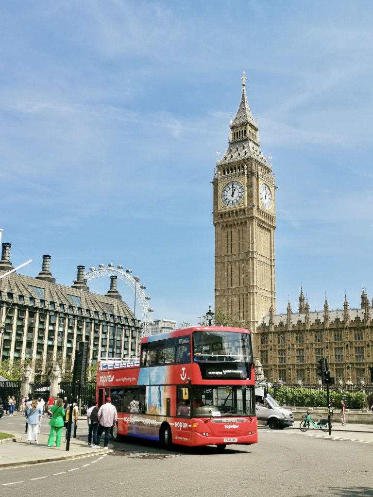 A red london bus driving in front of big ben in london as part of a london itinerary