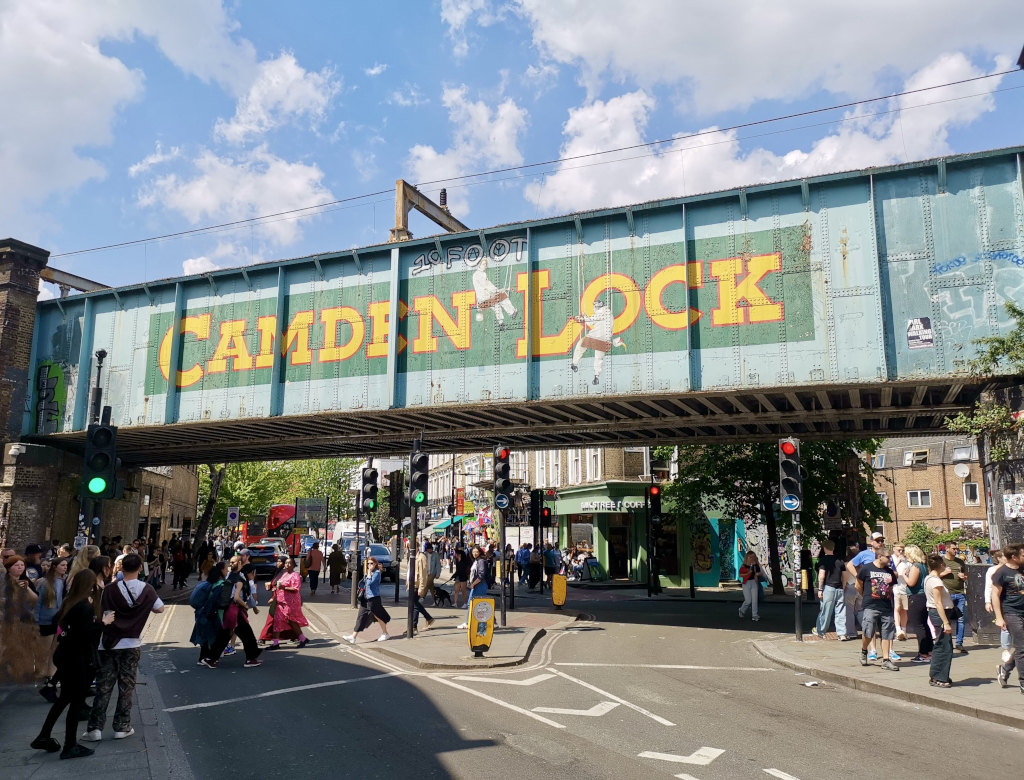 People walking across the street underneath a train bridge that says camden lock 