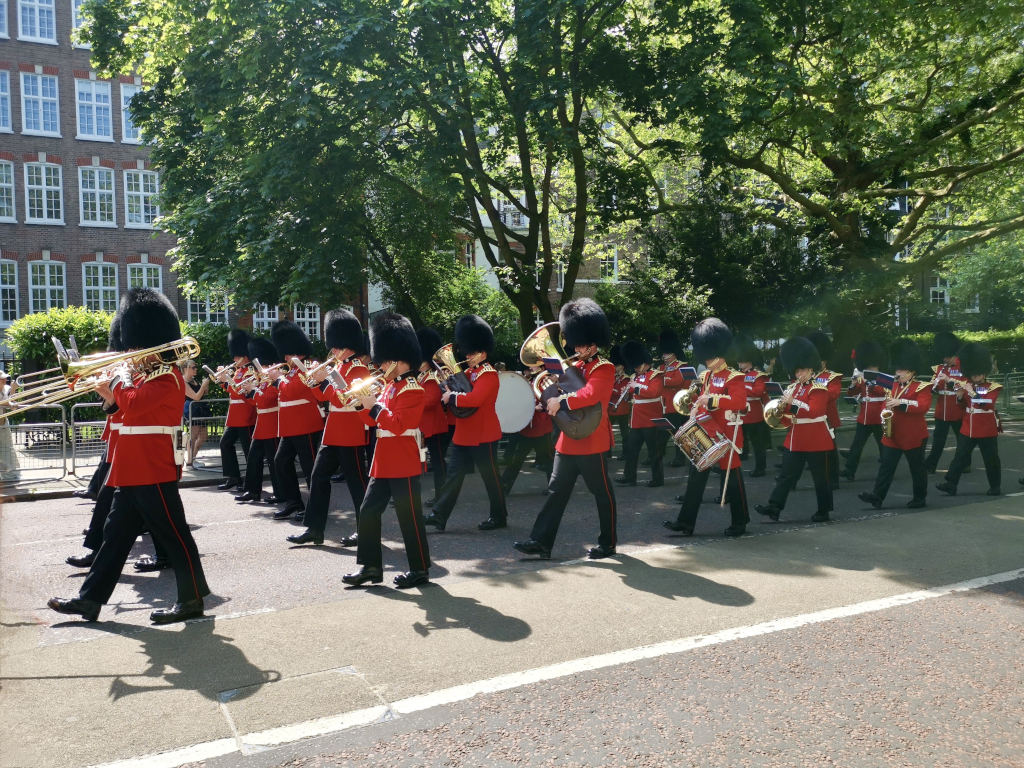 A group of guards dressed in traditional clothing marching down the road in London while playing instruments