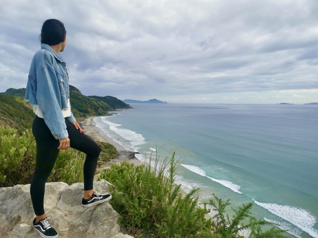 a woman standing on the top of a hill overlooking mangawhai beach on a northland road trip