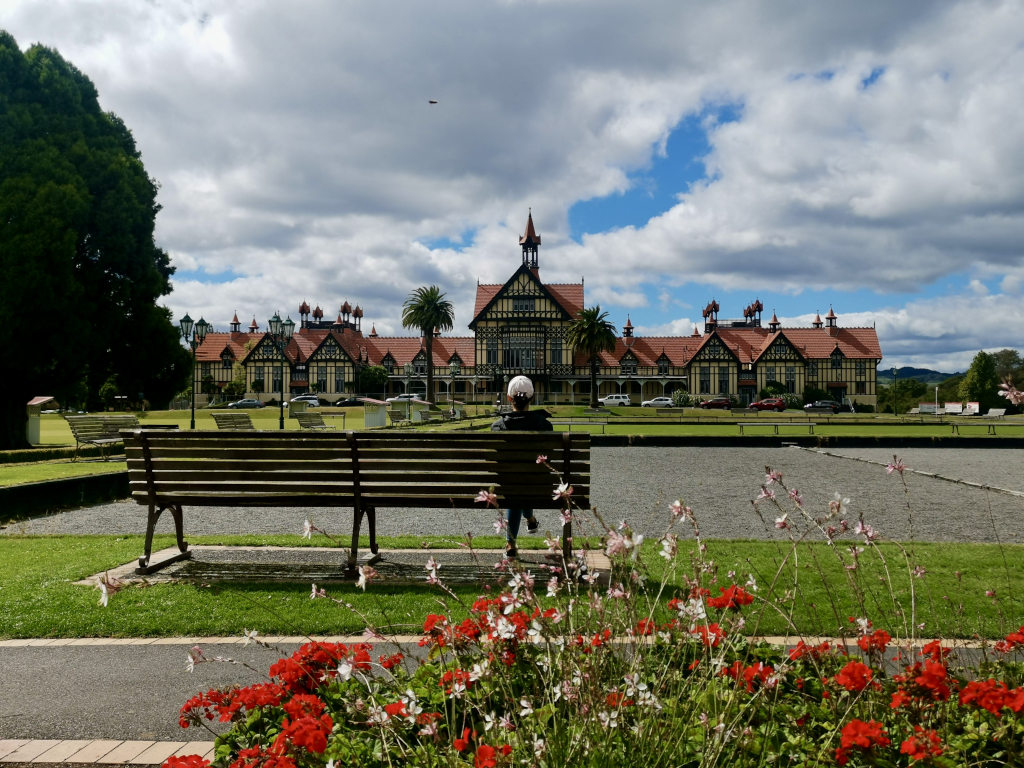 A woman sitting down at a park bench in front of the rotorua museum one of the best things to in in one day in new zealand