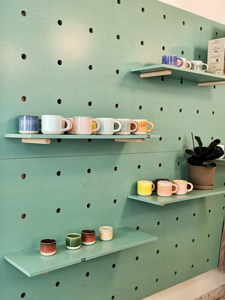 Several shelfs on an aquamarine coloured wall with different coloured coffee cups on them