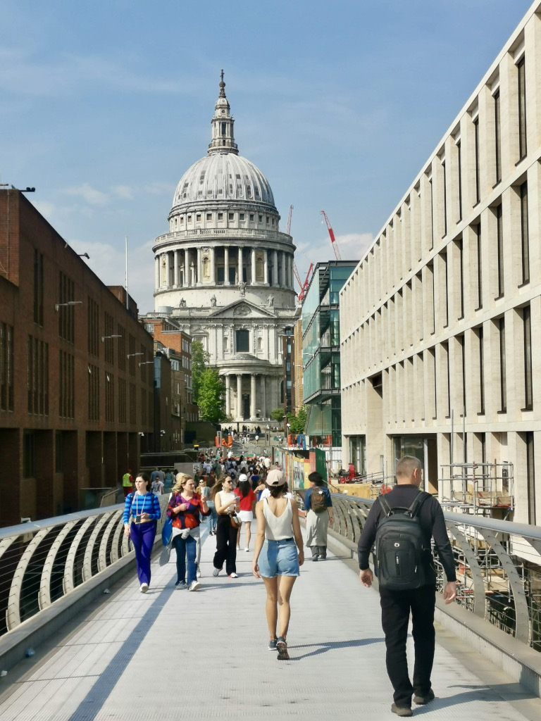 A group of people walking along the milennium bridge in London with St Pauls Cathedal in the background