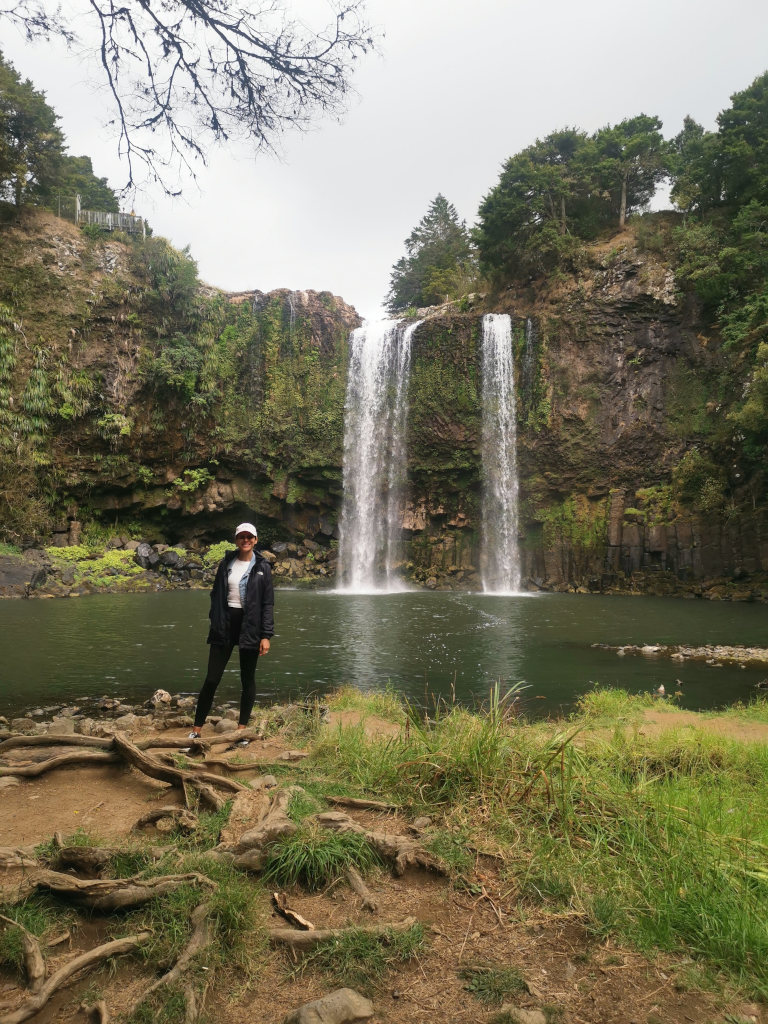 A woman standing in front of the whangarei falls during a northland road trip