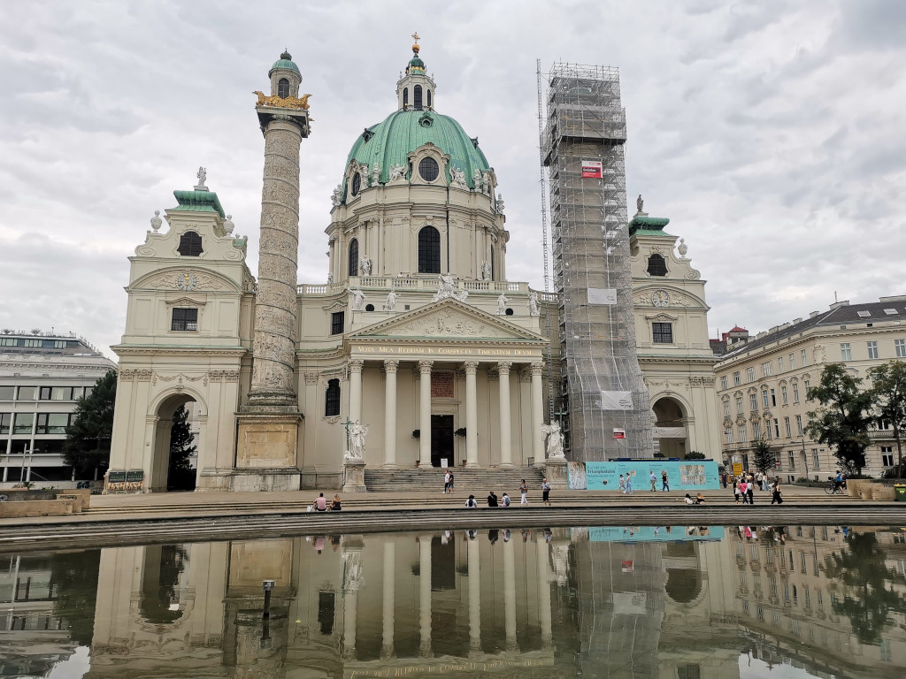 The st charles church in vienna with a pool reflecting the building in it the right hand spire of the chruch is under renovation