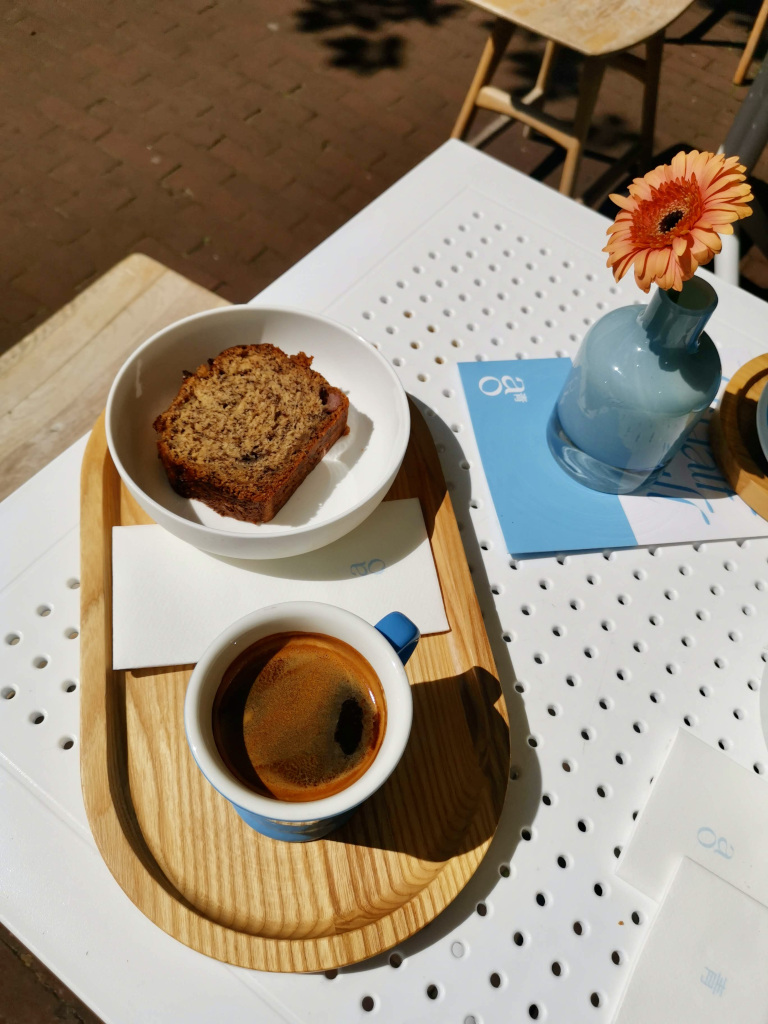 A cup of coffee with a piece of banana bread on a table with a orange flower at AO bar one of the best cafes in amsterdam