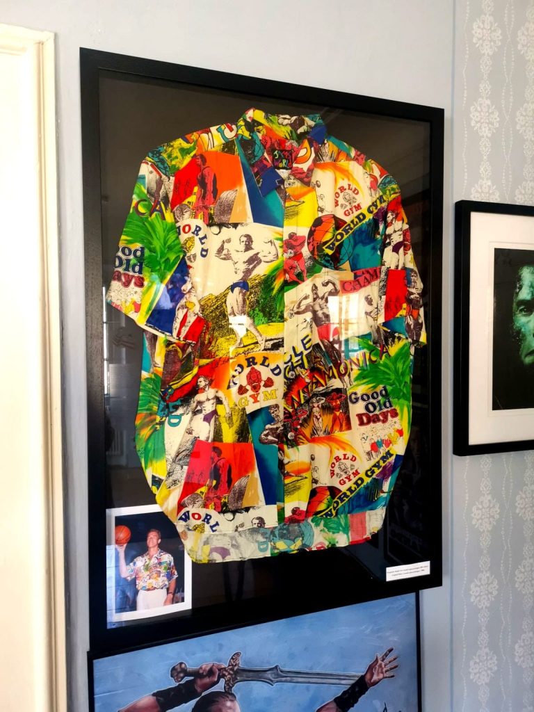 Colorful shirt framed in black with a photo of Arnold Schwarzenegger wearing it displayed beside, hanging on the wall of the Arnold Schwarzenegger Museum.