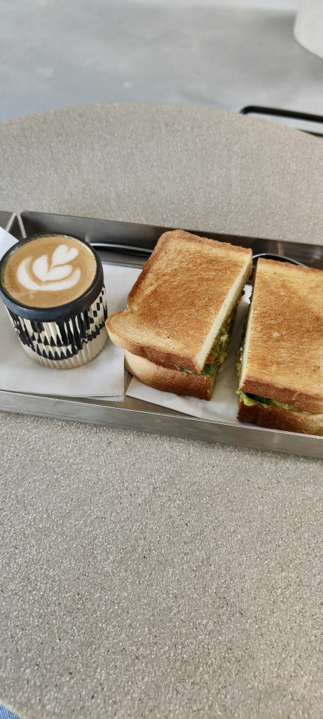 A cup of coffee sitting on a metal tray next to a toasted sandwich