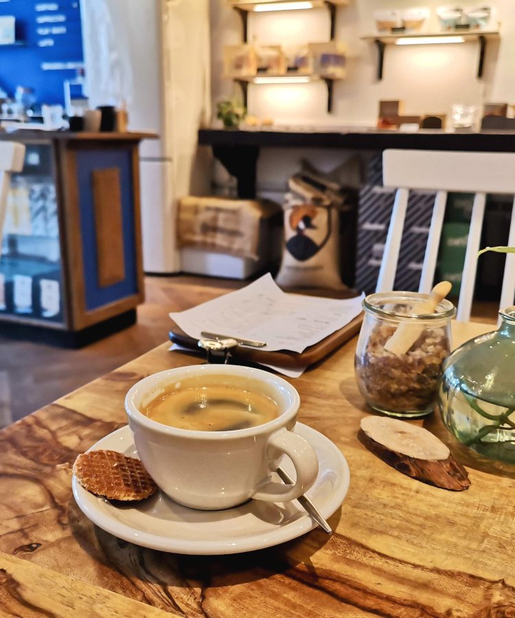 A black coffee in a white ceramic cup sitting on a wooden table in Sango Cafe, one of the best cafes in Amsterdam.