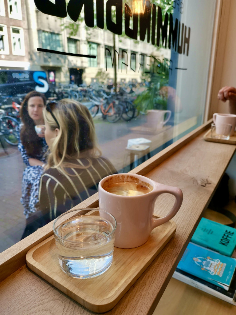 A cup of coffee sitting on a bench next to the window of hummingbird cafe one of the best cafes in amsterdam