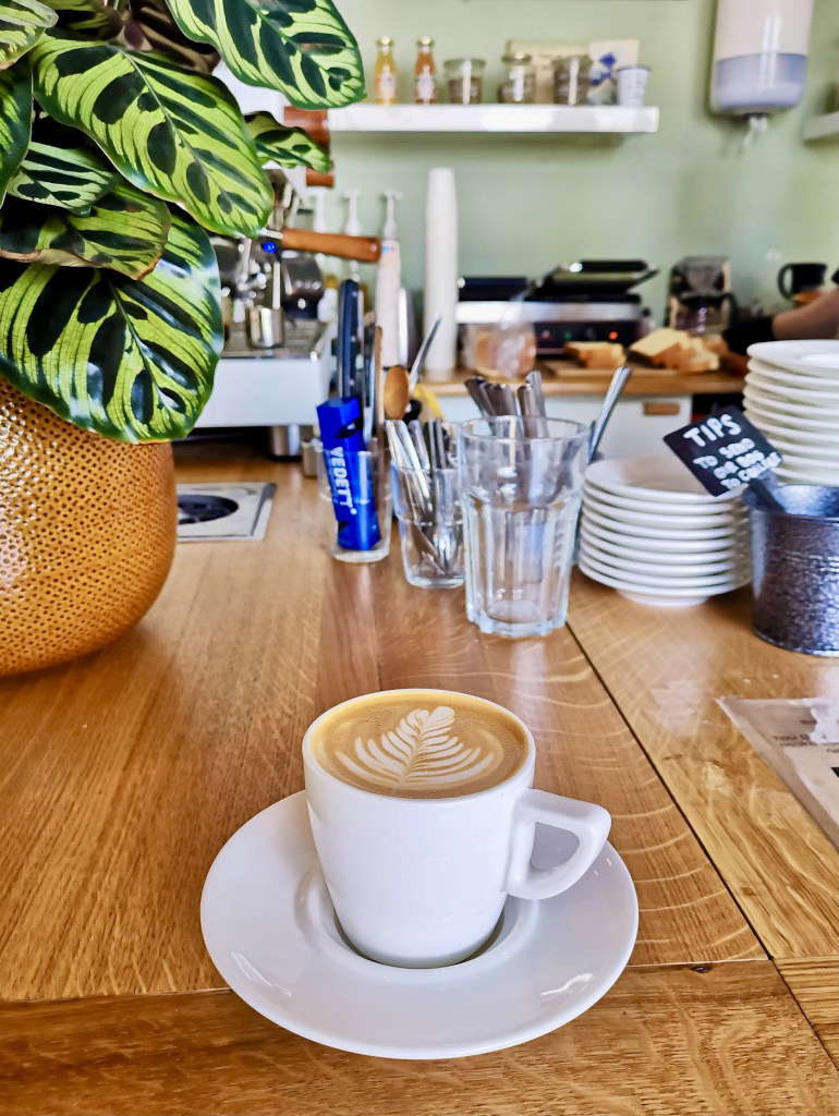 A flat white with beautiful coffee art in the cup sitting on a bench at gentle place cafe one of the best cafes amsterdam has to enjoy