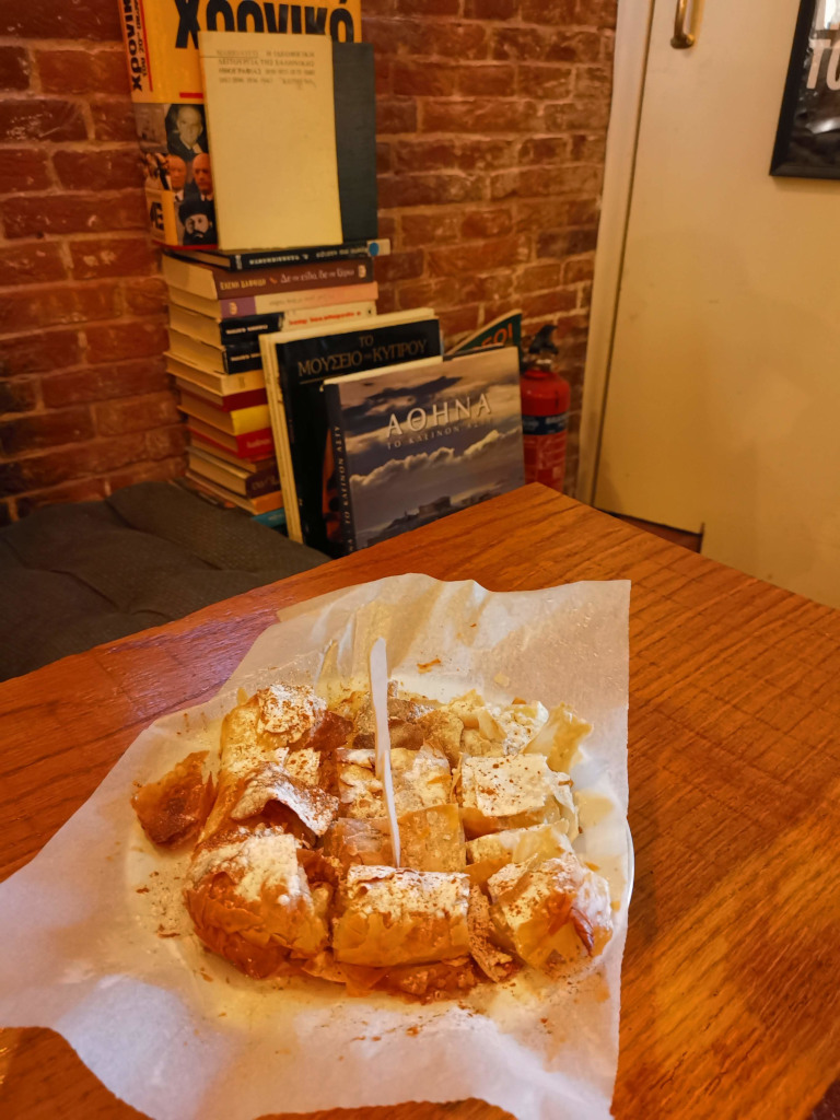 A greek pastry sitting on a table at a a cafe with a plastic for in it