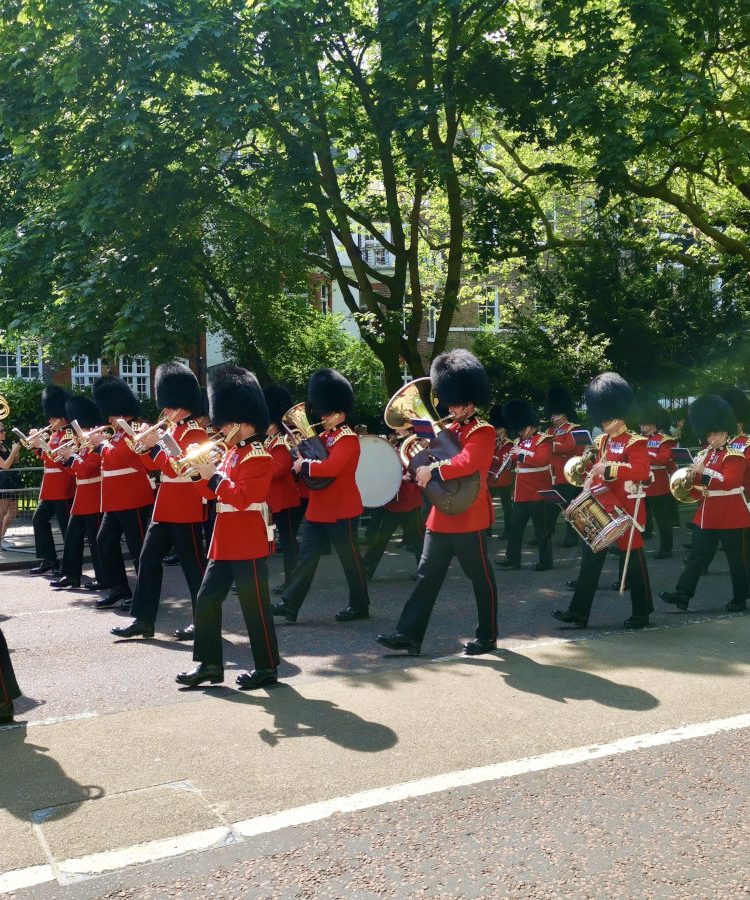 A group of london guards in traditonal uniforms marching down the street while playing instruments