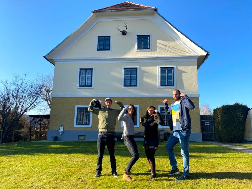 Allan, Katharina, and two friends posing outside the Arnold Schwarzenegger Museum, flexing their arm muscles in classic bodybuilder poses.