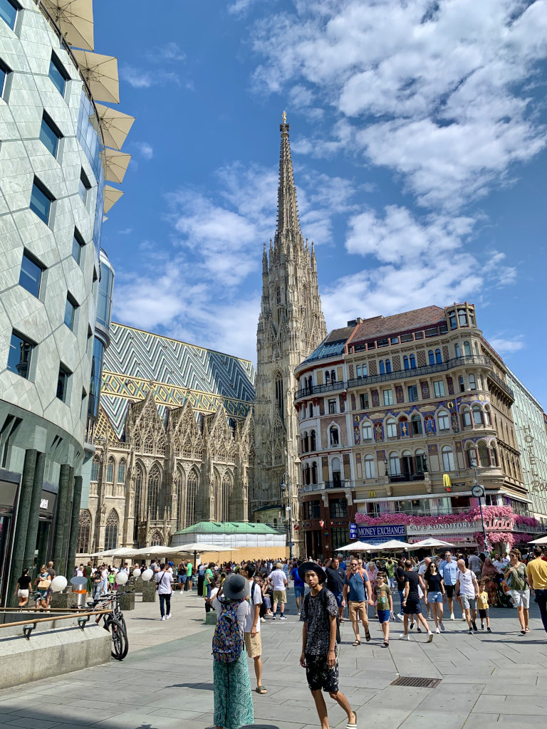 A sunny day in Vienna with many pedestrians walking in a square in front of st stephans cathedral