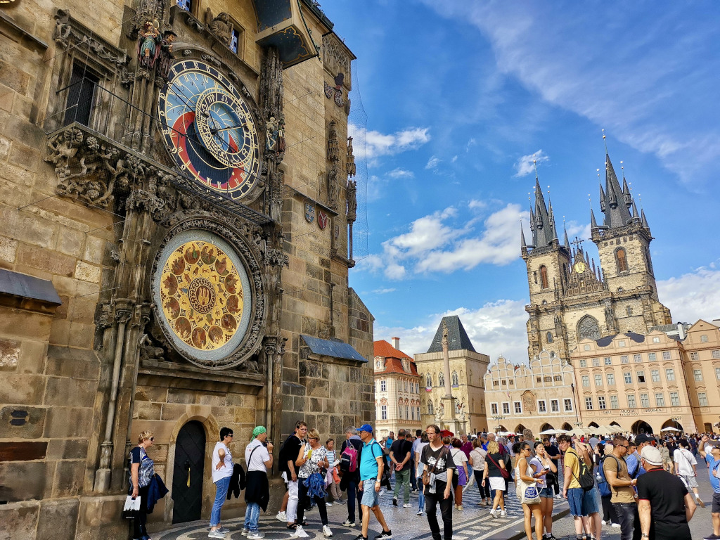 Groups of tourists gathering in the old town square of prague which is a good place to stop during a prague itinerary