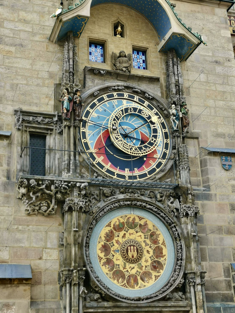 The colorful astronomical clock in prague that has a red and blue face and has small statues on either side of the clock face