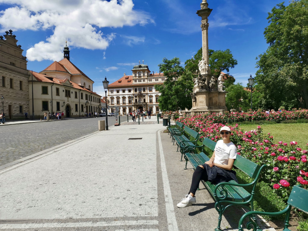 A woman in a white t-shirt and black jeans sitting on a green bench next to some flowers