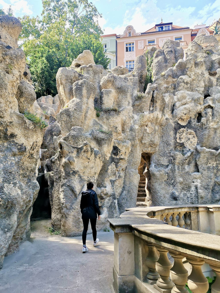 A woman walking along a walkway next to a grotto in a park in vinohrady prague