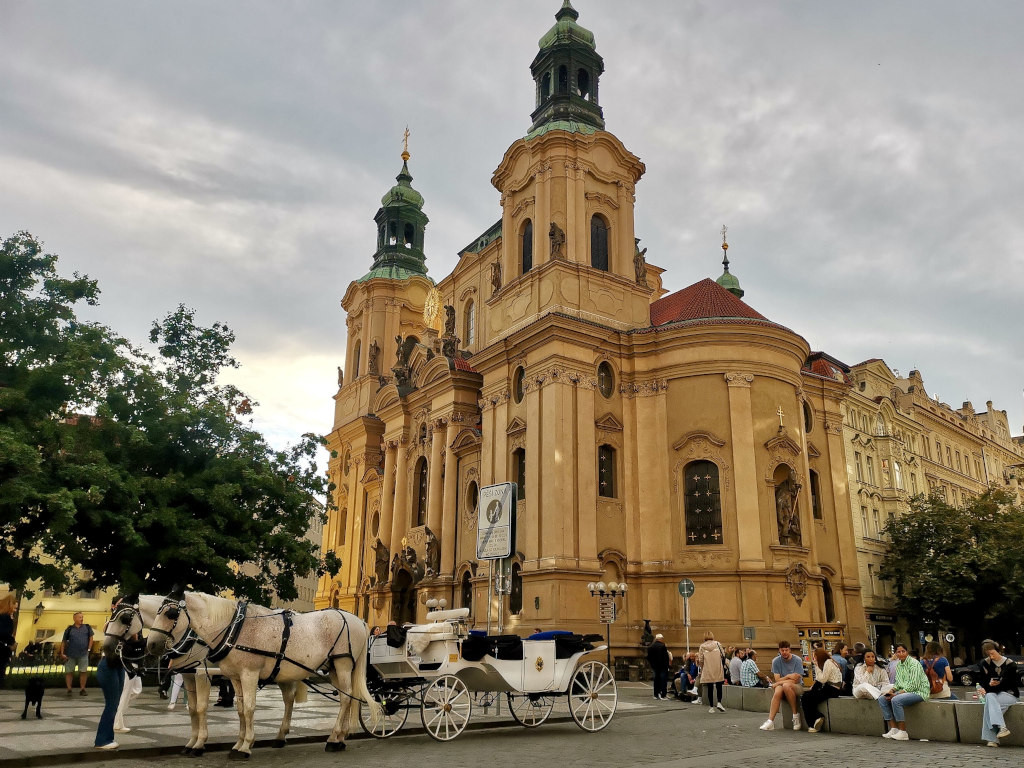 Two horses with a cart behind them outside of st nicolas church at the main square in prague