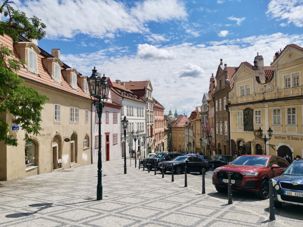 A street with colorful classical styled buildings in Prague with cars parked along the street 