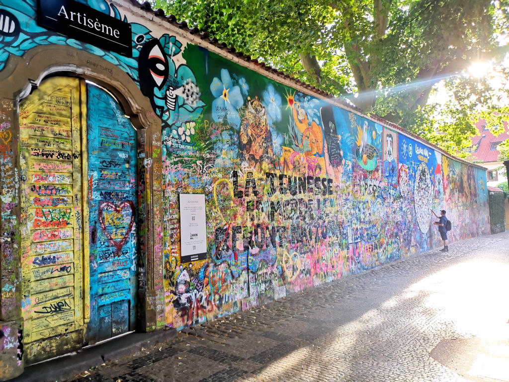 A man standing next to the jonh lennon wall in prague