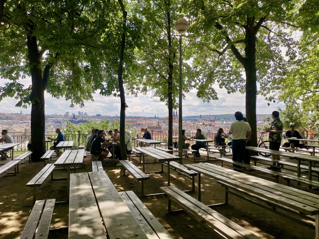 Some people sitting down at benches in a letna park beer garden a good stop on a prague itinerary