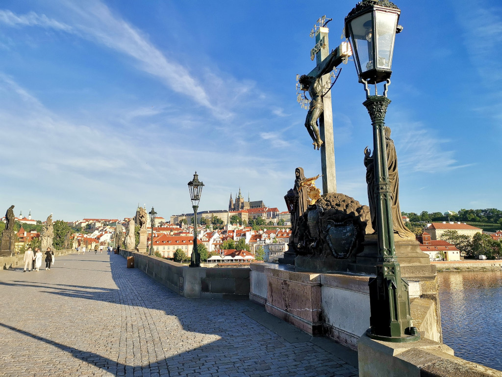 The charles bridge at sunrise in Prague with a few people walking across it a good place to visit on a prague itinerary