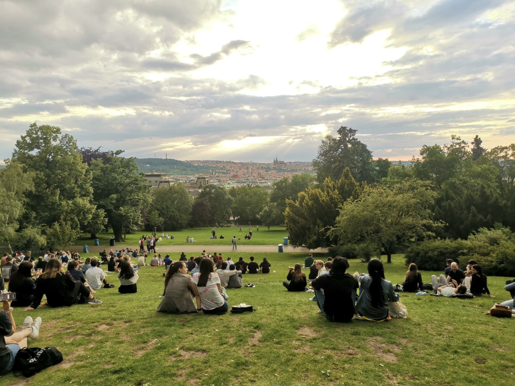 A crowd of people sitting in a park in prague watching the sunset over the old town after a prague itinerary exploring the city